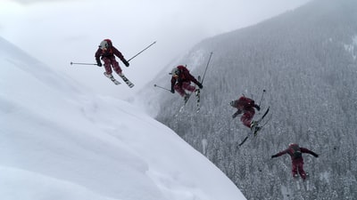 白天，穿着红色夹克和黑色裤子的人们在雪山上滑雪
